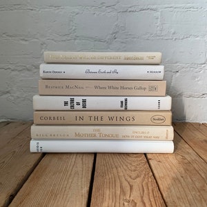 Peut inclure: Une pile de huit livres avec des couvertures blanches et des lettres dorées. Les titres incluent "This Year It Will Be Different", "Between Earth and Sky", "Where White Horses Gallop", "The Culture of Desire", "In the Wings", "The Mother Tongue", "English & How It Got That Way", et "Regis Ter".