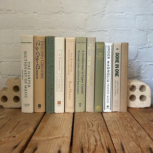 May include: A collection of 14 vintage paperback books with green and beige covers. The books are arranged in a row on a wooden surface. The titles of the books include "The Other Queen", "The 9 Steps to Financial Freedom", "A Gentlewoman in Upper Canada", "The Naked Aye", "Under Magnolia", and "Done in One".