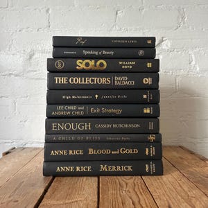 May include: A vertical stack of ten black hardcover books with gold lettering on the spines. The titles include Ref, Speaking of Beauty, Solo, The Collectors, High Maintenance, Exit Strategy, Enough, A Child of Bliss, Blood and Gold, and Merrick.