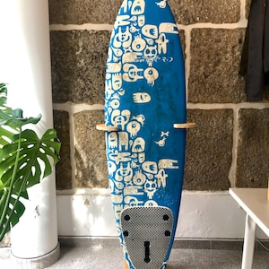 May include: A blue surfboard with a white graphic design of various cartoon characters. The surfboard is mounted on a wooden stand. The stand has the text "Rack-Co." printed on it. The surfboard has a black traction pad.