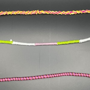 May include: Three different types of cord, each with a different color pattern. The top cord is yellow and red, the middle cord is green, white, and pink, and the bottom cord is black and pink.