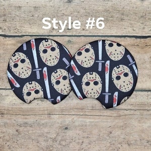 May include: Two car coasters with a black background featuring a pattern of a hockey mask and a bloody knife. The text "Style #6" is in white above the coasters. These coasters are designed to fit in a car's cup holder.