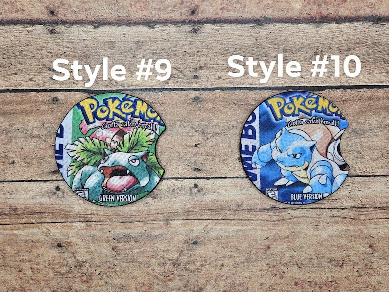 May include: Two round, colorful, printed, cardboard coasters with a Pokemon theme. The left coaster features a green version of the Pokemon character, Venusaur, with the text "Gotta catch 'em all!" and "Green Version". The right coaster features a blue version of the Pokemon character, Blastoise, with the text "Gotta catch 'em all!" and "Blue Version".