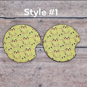 May include: Two yellow car coasters with a repeating pattern of Pikachu, a popular Pokemon character. The coasters are round and have a cut-out for a cup. Style #1.