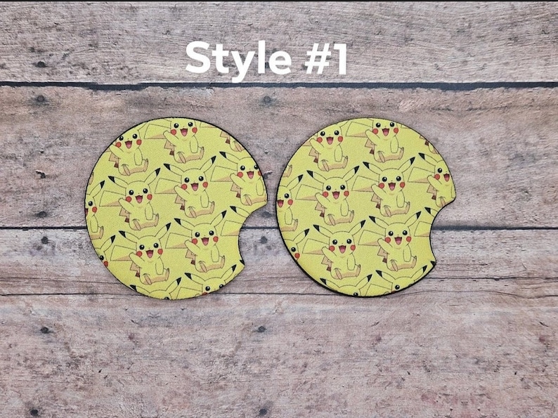 May include: Two yellow car coasters with a repeating pattern of Pikachu, a popular Pokemon character. The coasters are round and have a cut-out for a cup. Style #1.