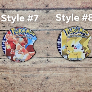 May include: Two round, printed, cardboard coasters. The left coaster features a red and blue Pokemon character with the text "Gotta catch 'em all!" and "Red Version". The right coaster features a yellow Pokemon character with the text "Special Pikachu Edition" and "Yellow Version".