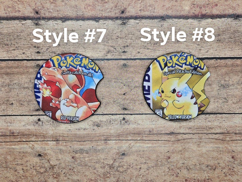 May include: Two round, printed, cardboard coasters. The left coaster features a red and blue Pokemon character with the text "Gotta catch 'em all!" and "Red Version". The right coaster features a yellow Pokemon character with the text "Special Pikachu Edition" and "Yellow Version".