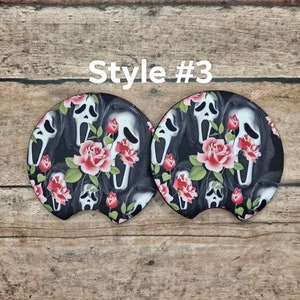May include: Two car coasters with a black background featuring white Scream masks and red roses. The text "Style #3" is in white. The coasters are designed to fit in a car's cup holder.