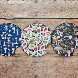 May include: Three round, fabric coasters with a mushroom and leaf pattern. The coasters are in blue, white, and brown.
