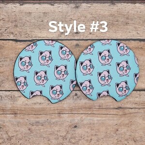 May include: Two round blue and pink car coasters with a repeating pattern of a cartoon pink Pokemon character with blue eyes. The text "Style #3" is above the coasters.