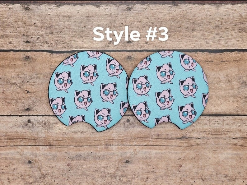 May include: Two round blue and pink car coasters with a repeating pattern of a cartoon pink Pokemon character with blue eyes. The text "Style #3" is above the coasters.