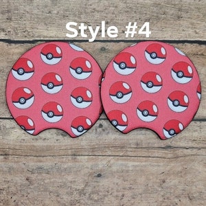 May include: Two red and white patterned drink coasters with a Pokeball design. The coasters are shaped like a car cup holder. Style #4.