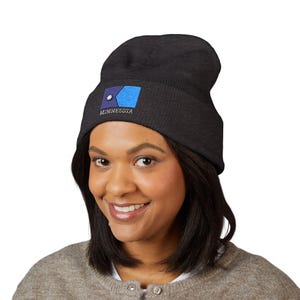 May include: A dark gray beanie with a ribbed texture. The front of the hat features an embroidered design of the Minnesota state flag, including a blue rectangle, a star, and the word "MINNESOTA".