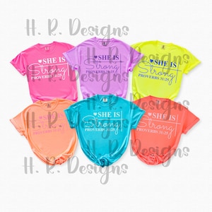 May include: A collection of six short-sleeved t-shirts in various colors, including pink, purple, yellow, orange, teal, and coral. Each shirt features the text "SHE IS Strong" with "PROVERBS 31:25" below it.