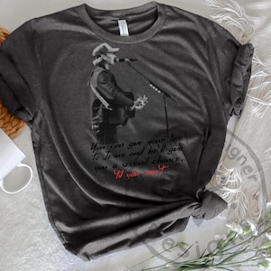 Puede incluir: Camiseta gris oscuro con una imagen en blanco y negro de un músico tocando la guitarra y cantando. La camiseta tiene el texto: "You can give your life to Jesus and He'll give you a second chance, 'Til you see it."