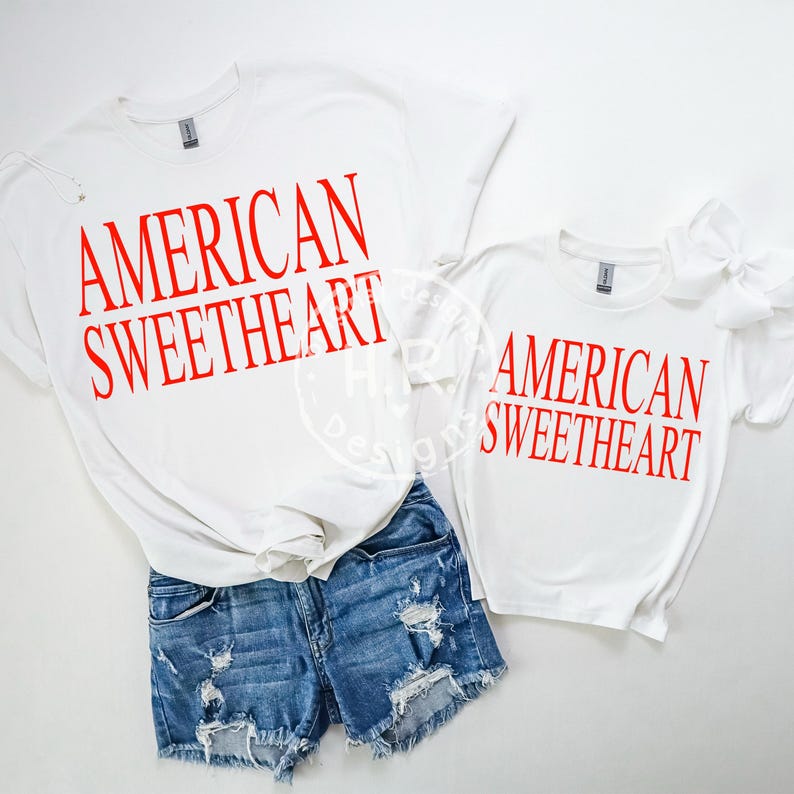 May include: White t-shirts with the text "AMERICAN SWEETHEART" in red. One shirt is paired with denim shorts. A smaller shirt with the same text and a white bow is also visible. The shirts are a casual style.