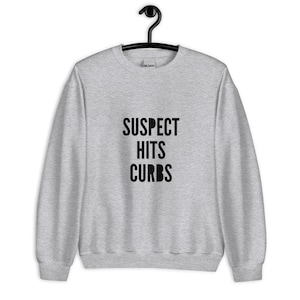 Puede incluir: Una sudadera gris jaspeada con el texto "SUSPECT HITS CURBS" impreso en negro.