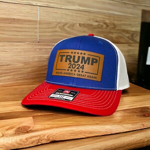 May include: A blue and white trucker hat with a brown leather patch that says "TRUMP 2024" and "MAKE AMERICA GREAT AGAIN".