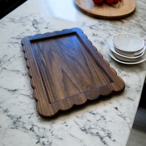 May include: A dark brown wooden serving tray with a scalloped edge sits on a white marble countertop.