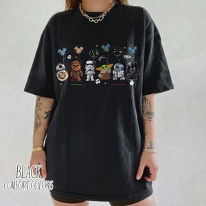 Op de afbeelding: Zwart comfort colors T-shirt met een afbeelding van Star Wars-personages die ballonnen vasthouden. De personages zijn BB-8, Chewbacca, een Stormtrooper, Grogu, R2-D2 en Darth Vader. De tekst "BLACK COMFORT COLORS" staat onderaan.