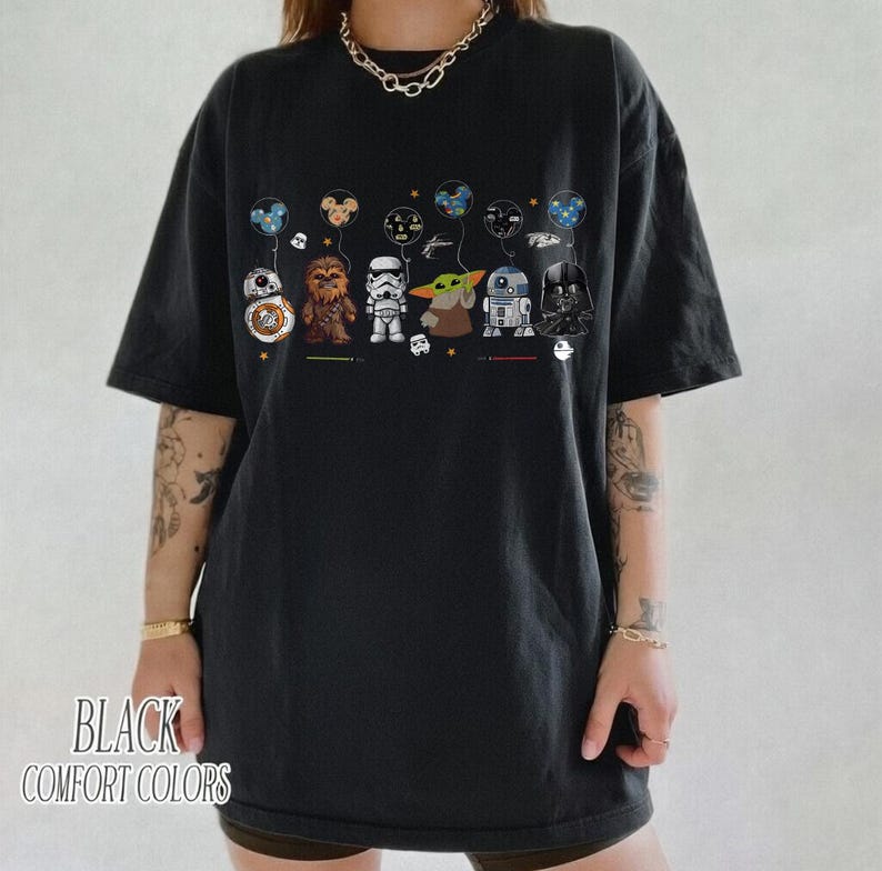 Op de afbeelding: Zwart comfort colors T-shirt met een afbeelding van Star Wars-personages die ballonnen vasthouden. De personages zijn BB-8, Chewbacca, een Stormtrooper, Grogu, R2-D2 en Darth Vader. De tekst "BLACK COMFORT COLORS" staat onderaan.