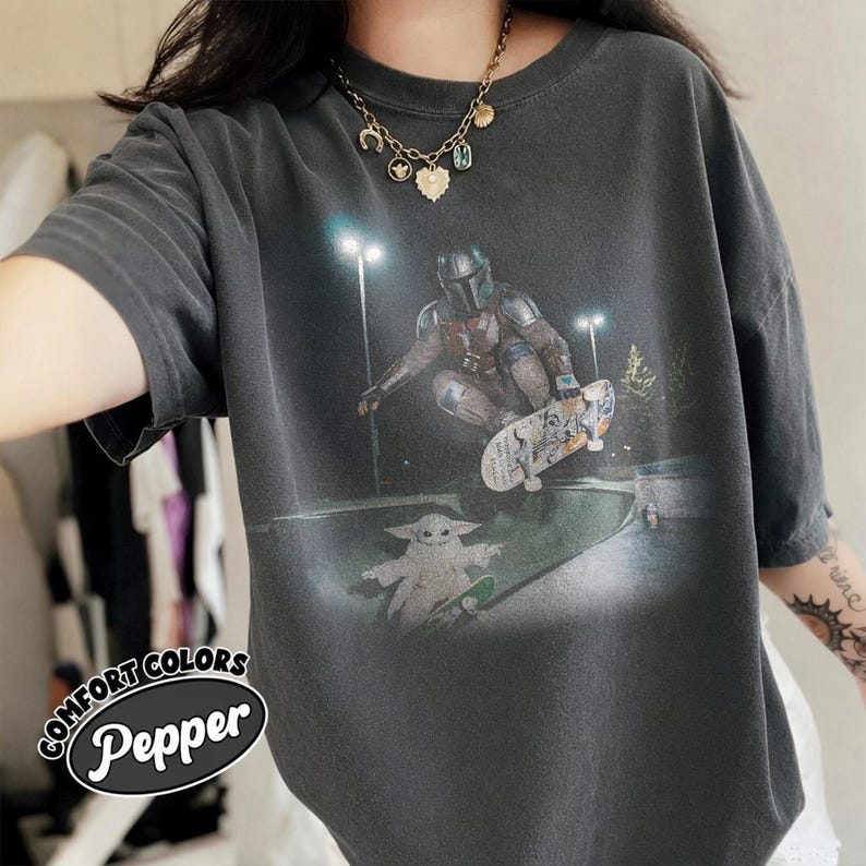 May include: Dark gray Comfort Colors t-shirt featuring a graphic of The Mandalorian skateboarding with Grogu. The design is set in a skate park at night. The shirt has the text "Pepper" and "Comfort Colors" in a circular design.