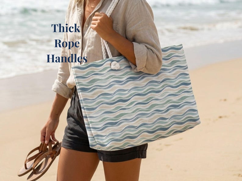 May include: A large tote bag with a wave pattern in shades of blue, green, and beige. The bag has thick rope handles and the text "Thick Rope Handles" is visible. The bag is being held on a beach.