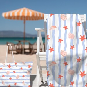 May include: Beach-themed set featuring a tote bag and a towel with a blue and white striped pattern. The pattern includes red starfish and light pink seashells. The items are on a white chair on a sandy beach with an orange and white umbrella.
