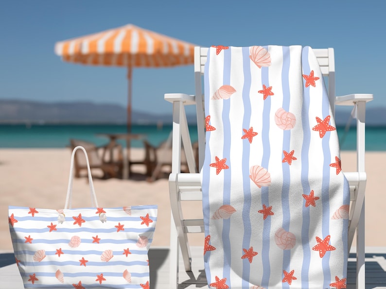 May include: Beach-themed set featuring a tote bag and a towel with a blue and white striped pattern. The pattern includes red starfish and light pink seashells. The items are on a white chair on a sandy beach with an orange and white umbrella.