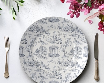 May include: A white ceramic plate with a blue toile pattern featuring figures, trees, and architectural elements. A silver fork and knife are on the right and left sides of the plate. Pink flowers and greenery are in the background.