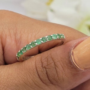 Puede incluir: Un anillo de banda de plata con una fila de piedras preciosas de esmeralda verde.