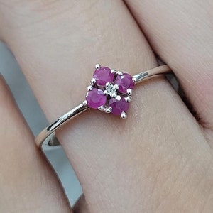 May include: A silver ring featuring a square cluster of pink gemstones. The ring is set with five pink gemstones, four of which are larger and arranged in a square shape, with a smaller gemstone in the centre.