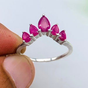 May include: A silver ring with a row of pink pear-shaped gemstones set in a curved arch design.