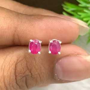 Może przedstawiać: Para srebrnych kolczyków z owalnymi, różowymi rubinami.