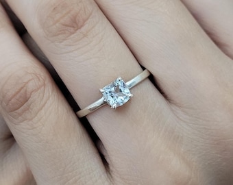 Op de afbeelding: Een zilveren ring met een heldere vierkante edelsteen.