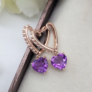 May include: A pair of rose gold heart-shaped earrings with dangling purple amethyst stones.