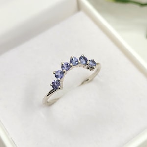May include: A silver ring with a row of small, light purple gemstones set in a curved arch shape.