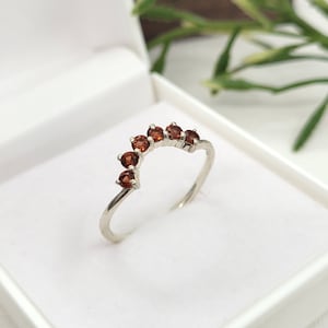 以下が含まれることがあります： 湾曲したアーチ型にセットされた、小さく丸い赤い宝石が並んだシルバーリングです。