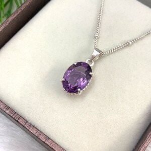 Pode incluir: Um colar de corrente de prata com um pingente oval de pedra preciosa roxa. O pingente &eacute; engastado em uma moldura de prata com uma borda decorativa.