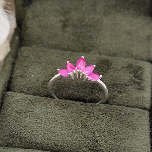 May include: A silver ring with a pink gemstone setting. The ring features a cluster of five pink gemstones in a flower shape.
