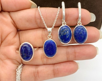 Puede incluir: Un conjunto de collar, anillo y pendientes de plata con piedras de lapislázuli ovaladas. Las piedras son de color azul intenso con motas doradas.
