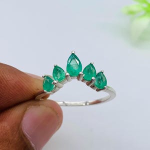 Pode incluir: Anel de prata com cinco esmeraldas verdes em forma de pêra. As pedras estão dispostas em arco, assemelhando-se a uma coroa. Uma joia elegante e original, com esmeraldas de um verde vibrante.