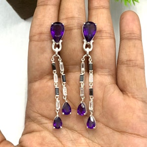 May include: A pair of dangle earrings with amethyst pear-shaped gemstones and black and white cubic zirconia stones.