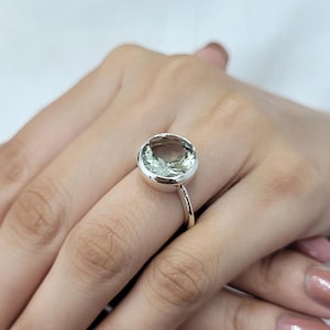 Può includere: Un anello d'argento con una grande pietra preziosa rotonda di colore verde chiaro.