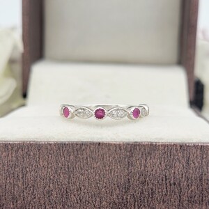Op de afbeelding: Een zilveren bandring met vijf rode edelstenen en kleine witte edelstenen in een delicaat ontwerp.