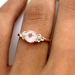 Könnte beinhalten: Ein Ring aus Roségold mit einem großen rosafarbenen Edelstein, der von kleineren weißen Edelsteinen umgeben ist.