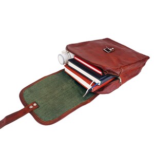 May include: A brown leather satchel with a flap, open to reveal a green interior and several books. A white cylindrical object is also inside. The bag has a metal clasp and a zipper closure.