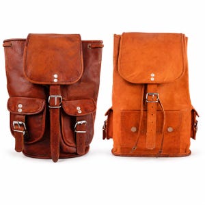 May include: Two leather backpacks in different shades of brown. The left backpack is dark brown with two front pockets and silver buckles. The right backpack is a lighter tan color with a single front pocket and a central strap with a silver buckle.