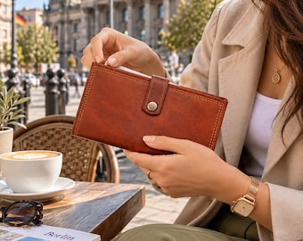 May include: A rectangular brown leather wallet featuring visible stitching along the edges and a central snap button closure. The wallet has a smooth, matte finish and is held in a horizontal position, showcasing its structured design and simple flap.