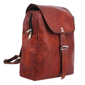 May include: A brown leather backpack with a flap closure and adjustable buckle. The backpack features a zippered front pocket and adjustable shoulder straps. The leather has a distressed appearance, and the hardware is silver-toned.